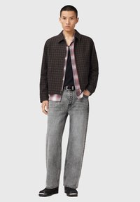 Veste noire texturée, chemise à carreaux rouges, t-shirt noir, jeans larges gris, chaussures noires avec accents argentés. Fond uni.