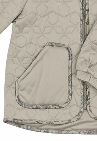 Veste matelassée beige avec un motif géométrique, ornée d'un accent floral sur le col et les bords des poches. Comprend une fermeture éclair et des poignets élastiques.