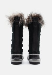 Bottes d'hiver en suède noir avec un bord en fausse fourrure sur le dessus, semelles en caoutchouc et coutures verticales. Présente le logo Sorel au niveau du talon.