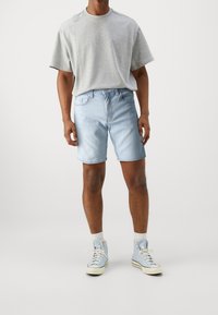 Šedé tričko s krátkým rukávem, světle modré džíny, a světle modré vysoké tenisky. Bavlněný materiál s volným střihem.