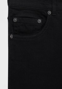 Jeans de mezclilla negra con un bolsillo frontal con remaches plateados y detalles de costura en contraste. La tela tiene una textura suave y mate.