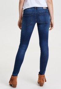 Jeans ajustados de denim azul oscuro, con una cintura de altura media, dos bolsillos traseros y una textura suave. Combinados con botas de tobillo color marrón claro.