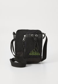 Bolso cruzado negro texturizado con correa ajustable, bolsillo frontal con cremallera y logo verde de Adidas. Fabricado con material duradero y diseño compacto.