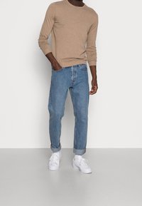 Beige pletený top s dlouhým rukávem v kombinaci se světle modrými volnými džíny s ohrnutými rukávy a bílými teniskami. Jednoduchý design, jemná textura a uvolněný střih.