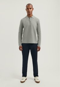 Grijze polo met lange mouwen en een drie-knopenhals, gecombineerd met marineblauwe broek en witte sneakers. Eenvoudig ontwerp, zachte textuur en reguliere pasvorm.