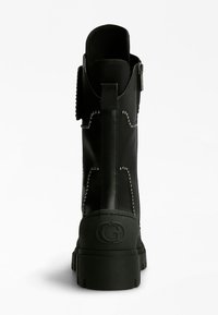 Botín negro de cuero liso con tachuelas metálicas a lo largo de las costuras, con una suela gruesa y un logo en el talón.