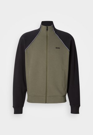 Μπουφάν με φερμουάρ σε ελιά πράσινο και μαύρο, με ψηλό γιακά, πλαϊνές τσέπες και λευκή επένδυση κατά μήκος των ώμων. Μαλακή υφή.