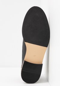Zapato negro con una suela de goma texturizada, material superior liso, acentos beige y tacón. Tamaño marcado como 37 en la suela.