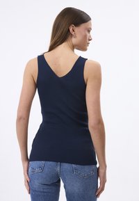 Tumed ribaga tank top V-kujulise seljaga. Selles on kitsad õlavarrevõrud ja nahkade kuju. Sobitatud helesiniste denimide teksadega.