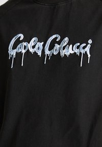 Zwarte sweatshirt met lichtblauwe geborduurde tekst in dripstijl die "Caplo Colucci" leest, met een accent op gedurfde ontwerpen en textuurcontrast.