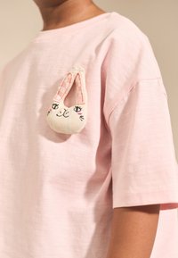 T-shirt di cotone rosa con vestibilità ampia, con una toppa a forma di coniglio sul petto con dettagli del viso ricamati e orecchie decorate.