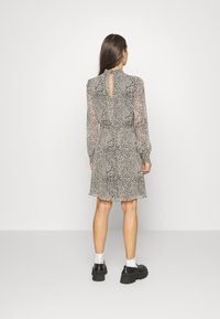 Vestido de estampado de leopardo em preto e bege, com mangas longas transparentes, decote alto e um detalhe em forma de buraco nas costas, finalizado com uma bainha rodada.