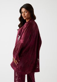 Bordeaux gemêlede kimono met bloemmotieven, brede mouwen en een satijnen afwerking. Draagt over bijpassende broek, met een vloeiende uitstraling.