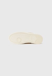 Könnyű bézs színű sneaker talp, gumiból készült, hullámos textúra mintázattal, középen kör alakú részlettel és kiemelkedő mintázattal.