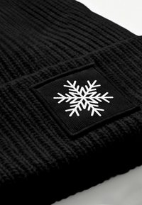 Black knitted beanie featuring a white snowflake emblem stitched on a square patch at the folded brim.