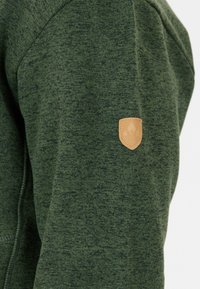 Felpa verde con un tessuto strutturato. Presenta una patch in pelle beige sulla parte superiore del braccio. Design semplice e vestibilità atletica.
