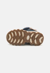 Kids wandelschoenen met een donkergroene bovenkant, een bontvoering, een textuur van bruine rubberen zool en witte accenten. Opvallend grippatroon op de zool.