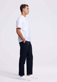 Witte katoenen T-shirt gecombineerd met marineblauwe denimbroek en witte sneakers. Eenvoudig ontwerp en pasvorm, toont een zijaanzicht van de outfit.