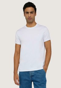 Camiseta de algodón blanca con cuello redondo, mangas cortas y un pequeño logo en el pecho, combinada con jeans de mezclilla azules.