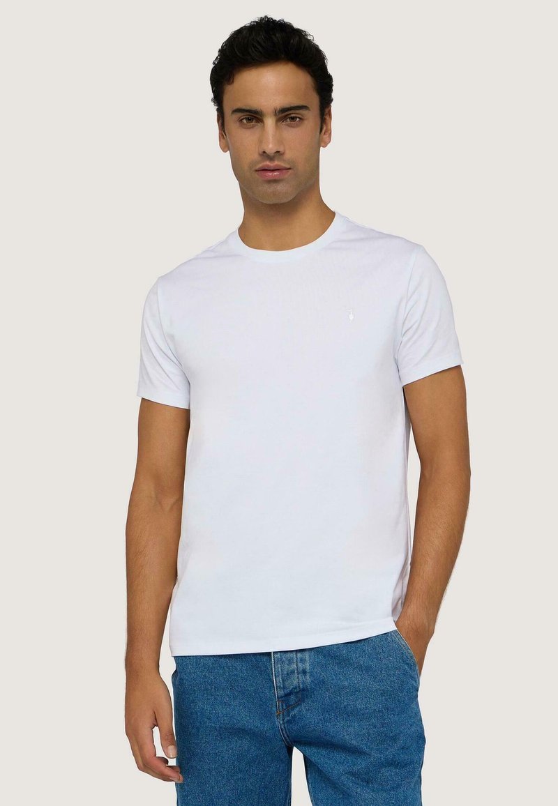 Camiseta de algodón blanca con cuello redondo, mangas cortas y un pequeño logo en el pecho, combinada con jeans de mezclilla azules.