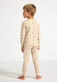 Beige ribota pidžamu komplekts bērniem, ar izkaisītiem ziedu un lapu rakstiem brūnā, zilā un oranžā krāsā. Elastīgi aproces pie rokām un kājām.
