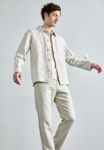 Chemise à rayures dans des tons crème et bleu foncé, avec une poche poitrine, portée avec un pantalon en lin clair. Style décontracté, coupe relaxée, tissu texturé.
