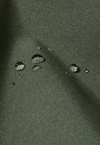 Tessuto verde testurizzato con gocce d'acqua visibili, che evidenziano la sua qualità resistente all'acqua e la superficie liscia.