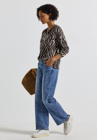 Lange mouwen top in beige met zwarte zebra strepen, gecombineerd met lichtblauwe relaxed-fit jeans, witte sneakers en een bruine tas.