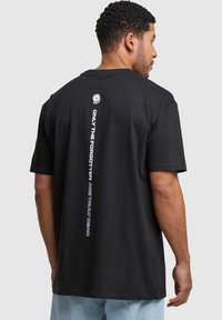 Sort bomulds T-shirt med runde hals, korte ærmer og et grafisk design på ryggen med hvid tekst og et lille accentlogo.