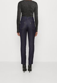 Mörkblå denimbyxor med hög midja, med bakfickor och guldtonade detaljer. Slät textur med skräddarsydd passform.