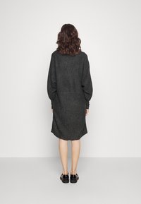 Grå ullklänning med avslappnad passform, sänkt axel och ribbad struktur. Har en rundad nederkant och medellång längd. Matchas med svarta skor.