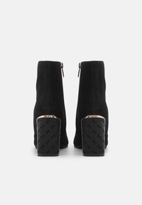 Bottines en suede noir à bout rond, avec fermeture éclair et un talon bloc texturé présentant un motif et un accent doré en haut.