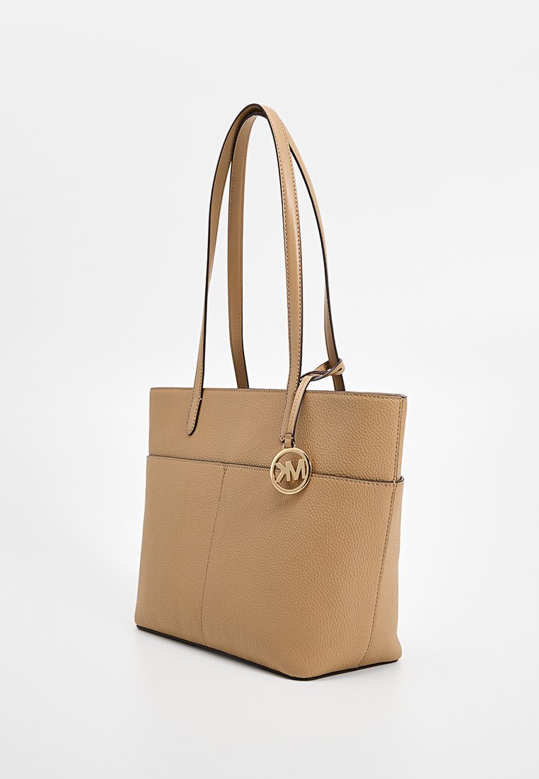 Borsa a tracolla in pelle beige con due manici lunghi, un accento con logo circolare dorato e una superficie testurizzata. Presenta una tasca anteriore.