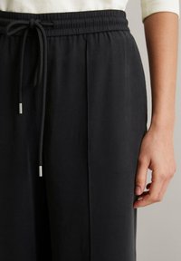 Schwarze Jogginghose mit elastischem Bund und Kordelzug. Mit silbernen Hardware-Akzenten und strukturiertem Gewebe für zusätzlichen Komfort.