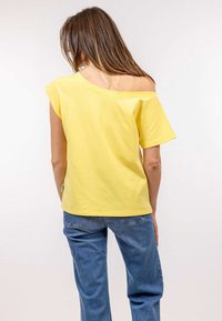 Žluté tri�čko s krátkým rukávem a designem bez ramínka, vyrobené z měkké bavlny. Vpárované s modrými džíny z denimu, které mají volný střih.