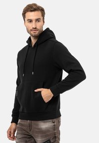 Schwarze Kapuzenjacke aus weichem Stoff, mit einer Kängurutasche, Kordelzugkapuze und gerippten Bündchen. Einfaches, unauffälliges Design.