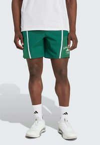 Shorts de sport verts avec des rayures blanches sur les côtés, arborant le logo sur la jambe gauche. Le matériau semble léger et respirant.