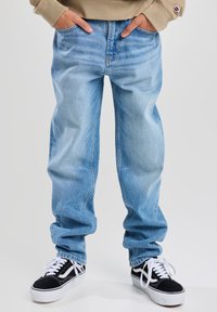 Jeans de mezclilla azul claro con un corte holgado y acentos desgastados, combinados con zapatillas bajas en negro y blanco con un acabado texturizado.