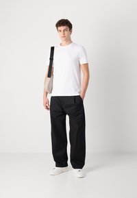 Witte kortemouw t-shirt, losse zwarte broek en witte sneakers. Het model draagt een beige tas met een zwarte band. Eenvoudig ontwerp en kleuren.