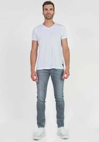 T-shirt blanc à manches courtes et à col en V, associé à un jean slim gris clair et des baskets blanches. L'ensemble présente un design décontracté.