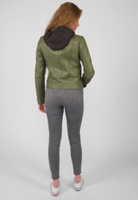 Olivgrön läderjacka med grå huva, figursydd design, synliga sömmar och silverfärgad detaljer. I kombination med grå smala jeans och vita skor.