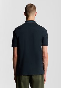 Polo shirt corto a maniche corte di color blu navy scuro con colletto piatto, caratterizzato da sottili strisce decorative vicino al collo e un tessuto semplicemente testurizzato.