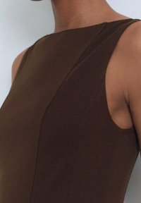 Haut marron sans manches en tissu côtelé, avec une coupe ajustée et des coutures inclinées, à la texture lisse.