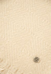 Tessuto crema a zigzag con una morbida texture e bordi frangiati, dotato di un pulsante decorativo con logo in argento.