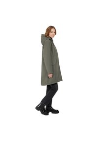 Impermeable verde oliva con capucha, con un diseño recto y grandes bolsillos laterales, combinado con jeans negros y botas negras gruesas.