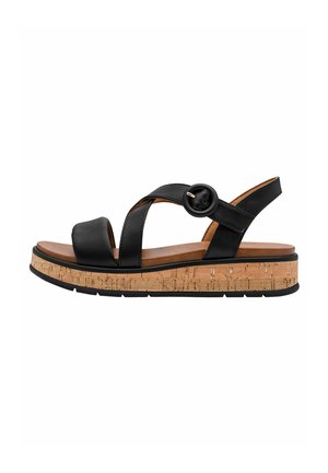 Sandale en cuir noir avec brides croisées, accent circulaire, plateforme en liège et semelle en caoutchouc texturée, offrant un design superposé et un bon maintien.