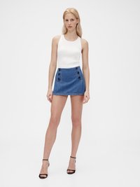 Vit ribbad linne topp som kombineras med en denim miniskirt med hög midja, fyrkantiga knappdetaljer och en fransad fåll. Svarta klacksandaler.