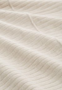 Getextureerde stof in zacht beige met subtiele golvende lijnen, die een zachte patroon over een glad oppervlak bieden en de geweven kwaliteit benadrukken.