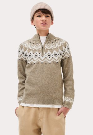 Khaki sweter z białymi i czarnymi geometrycznymi wzorami, zamek półdługi przy kołnierzy, ściągacze na rękawach i na dole. Jasnoróżowa dziana czapka. Beżowe spodnie.