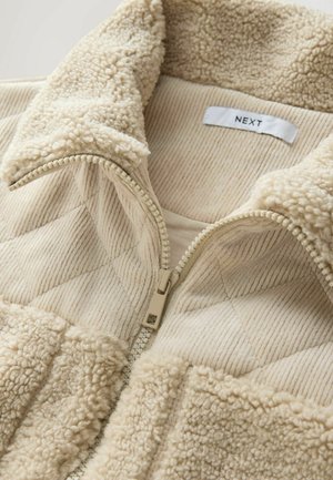 Beige lynlåsjakke med blød, fuzzy krave og kviltet tekstur. Har ribbet stof og kontrastfyldige fleece-detaljer. Mærke: NEXT.